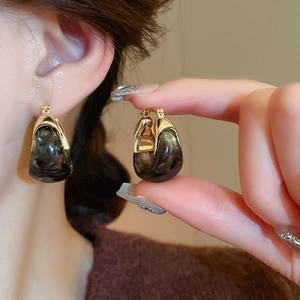 Macro detail of U-shaped golden resin earrings with marble texture on model's ear
