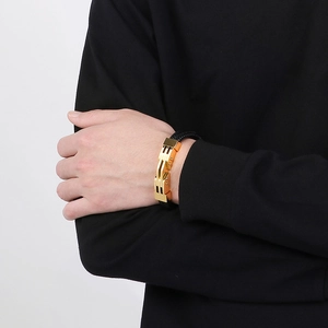 Dettaglio di un bracciale da uomo in pelle nera intrecciata con fibbia dorata