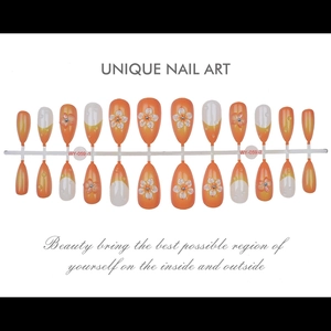 Détail de faux ongles en amande avec dégradé orange et motifs floraux blancs en relief