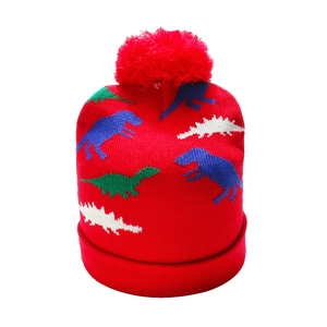 Detail of red knit kids hat with cartoon dinosaur pattern and soft fluffy pompom top