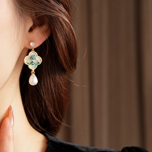 Détail de boucles d'oreilles fleur dorées avec émail vert et perle sur un mannequin