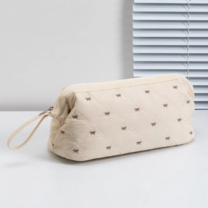 Detail of cream nylon travel bag with quilted diamond pattern and brown bow embroidery