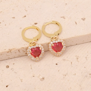 Detail of golden heart earrings with red gemstones on natural stone surface