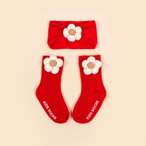 Détail d'un bandeau et de chaussettes bébé rouges avec fleurs 3D et semelle antidérapante