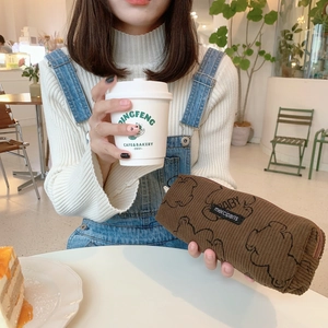 Close-up of brown corduroy pencil case featuring black bear print and woven labels