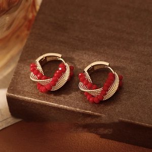 Twisted gold hoop earrings with red crystal beads shown on a vintage wooden surface