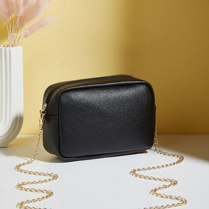 Elegant black embossed crossbody bag with golden chain strap on a modern tabletop