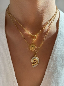 Close-up of layered gold necklaces with sun disc and spiral shell pendants on a model
