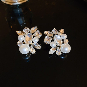 Detail of elegant gold earrings with faceted crystals and white faux pearls on black surface