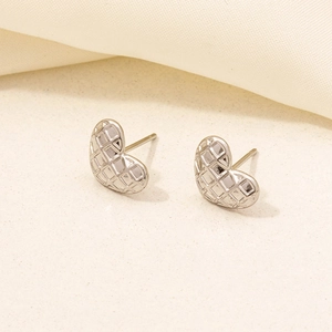 Macro detail of silver heart stud earrings with quilted texture on cream fabric