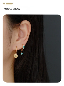 Close-up of model wearing gold huggie earrings with turquoise beads and sun charm