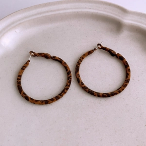 Detail view of large leopard print hoop earrings in brown tones on a ceramic plate