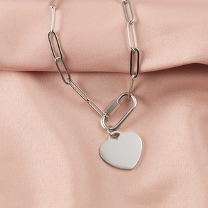 Macro shot of silver paperclip chain necklace with a polished heart pendant on pink silk