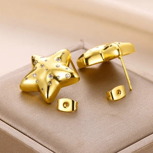 Detailed view of gold star-shaped stud earrings with sparkling cubic zirconia on fabric