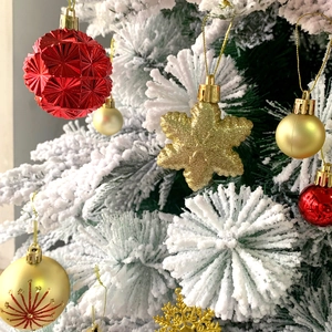 Detail of red and gold Christmas ball ornaments with snowflake pendants on snowy tree