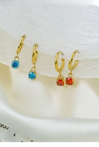 Macro shot of gold geometric earrings with blue and orange cubic zirconia on silk cloth