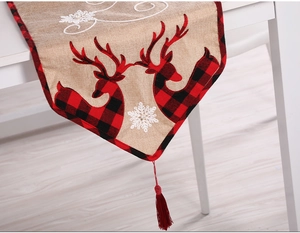 Detail of Christmas table runner with red plaid trim, reindeer pattern, and red tassel