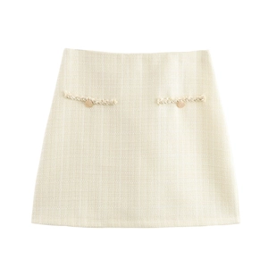 Détail de jupe trapèze en tweed beige avec boutons dorés et franges sur les poches