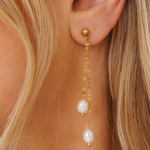 Close-up of dual gold chain tassel earrings with baroque pearls on model's ear