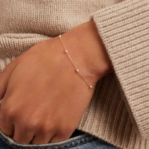 Detalle de una pulsera de perlas de cadena dorada sobre un jersey de punto beige