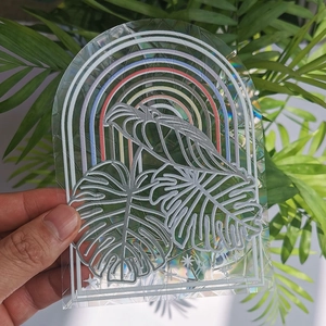 Close-up of holographic monstera leaf suncatcher sticker held over green plants