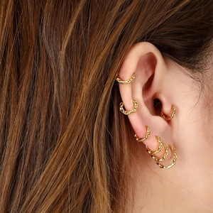 Detail of multiple gold chain-textured hoop earrings worn on a model's ear lobe and cartilage