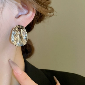 Close-up of irregular silver-toned wrinkled metal earring worn on earlobe for detail