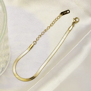 Detail shot of golden flat snake chain bracelet with K18 tag on white silk backdrop