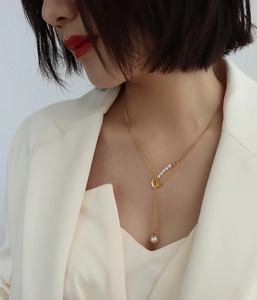 Detailed view of gold pin necklace with pearl fringe tassel and 18k finish on model