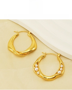 Detail of gold twisted hoop earrings with white pearls on a soft silk fabric background