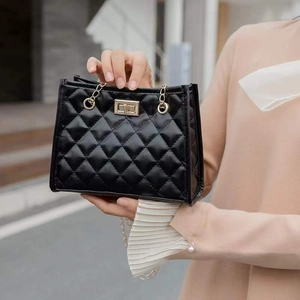 Elegante schwarze Stepptasche mit goldener Kette, getragen von einem Model auf der Straße