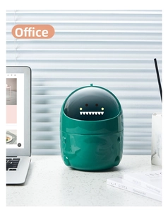 Close-up of a green dinosaur desktop trash can used in a modern office desk setting