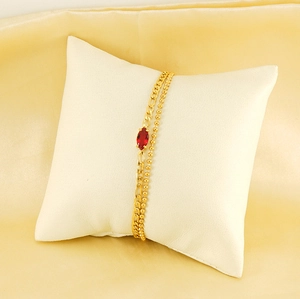 Close-up of gold double-layer bracelet with red marquise stone on a beige display pillow
