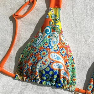 Close-up of vibrant paisley print bikini top with bright orange straps and knit texture