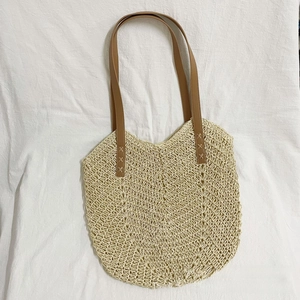Detail of hand-woven paper straw tote with brown faux leather strap and cross stitching