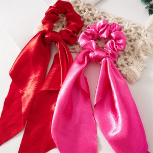 Detail of red and pink satin scrunchies with long ribbons on a minimalist woven mat