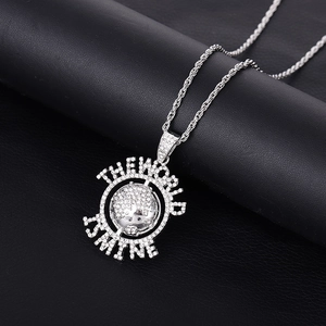 Gros plan du pendentif planète argentée avec gravure THE WORLD IS MINE et cristaux brillants