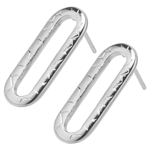 Macro detail of silver oval stud earrings with engraved star patterns on steel surface