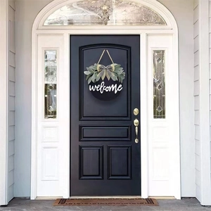 Close-up of black round welcome sign with white letters, green plants and buffalo plaid bow