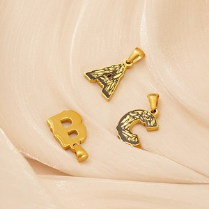 18k vergoldete Edelstahl-Buchstabenanhänger A, B und C auf weichem beigem Seidenstoff