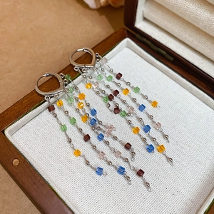 Close-up of colorful beaded tassel earrings with silver clasps on a vintage wooden jewelry box