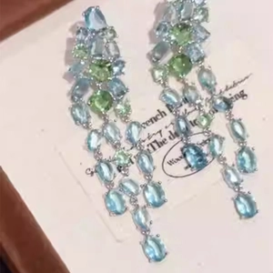 Macro detail of geometric oval tassel earrings with light blue and green zircon stones
