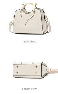 Detail view of white handbag featuring cat-ear gold handles and protective base studs