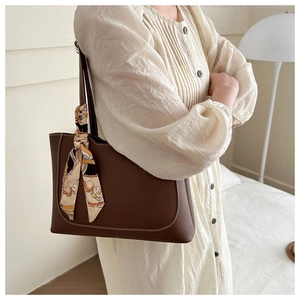 Détail d'un sac cabas marron avec poignée en foulard de soie porté sur robe blanche