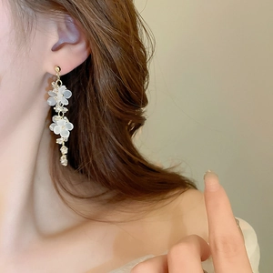 Close-up of elegant gold tassel earrings with white frosted flowers and tiny crystals