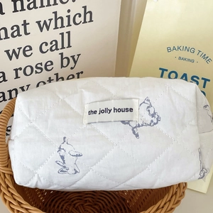 Quilted white cotton cosmetic bag with blue rabbit prints in a rustic woven basket