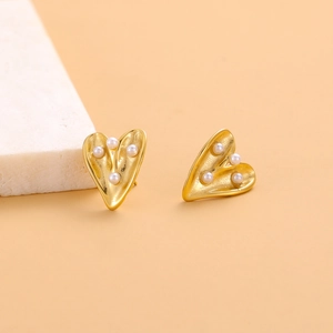 Detailed macro shot of golden heart stud earrings with inlaid pearls on marble