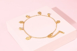 Detailed view of a gold clover anklet with small bells on a pink geometric stand