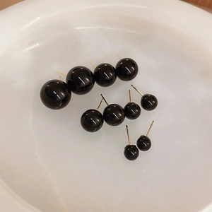 Detailed comparison of various sizes of black spherical stud earrings in a white bowl