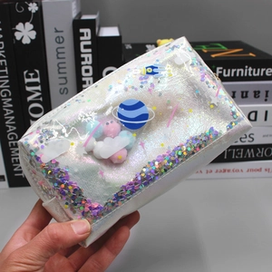 Macro shot of silver laser PVC cosmic makeup bag with glitter planets and colorful pom-poms